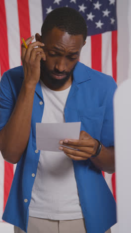 Vertical-Video-Shot-Of-Man-Next-To-Booth-With-Ballot-Paper-In-American-Election-Deciding-How-To-Cast-His-Vote-3